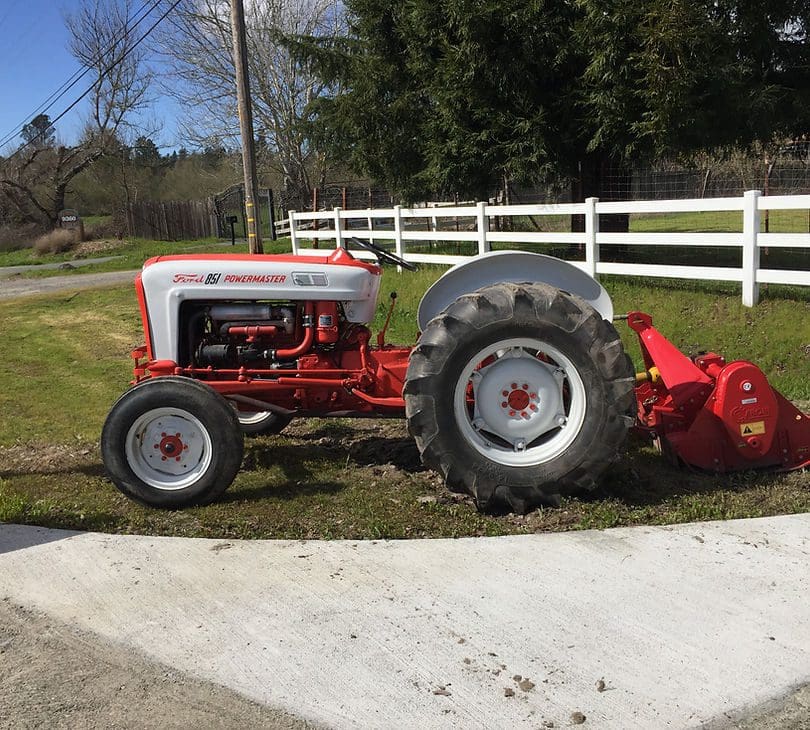 A red tractor parked in the grass near a fence.