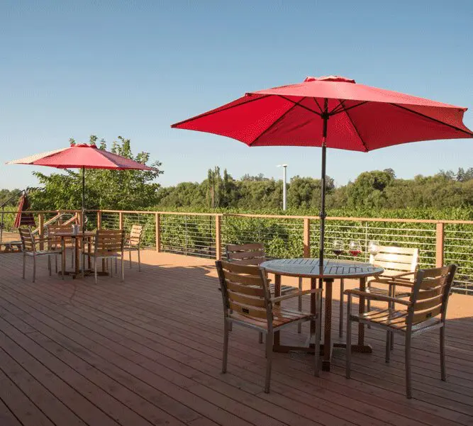 A deck with tables and chairs, two umbrellas.