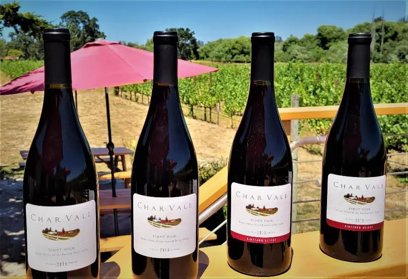 Four bottles of wine on a table in front of some trees.